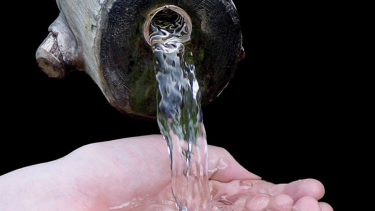 Wasser rinnt aus einem Holzrohr in eine Hand.