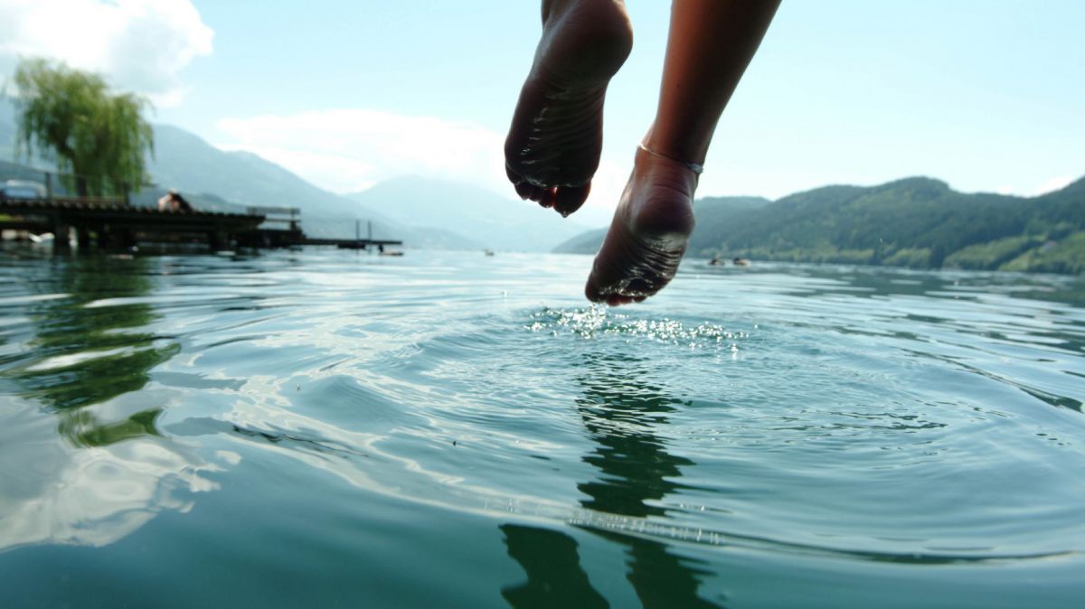 Füsse baumeln von einem Steg in das Wasser eines Sees