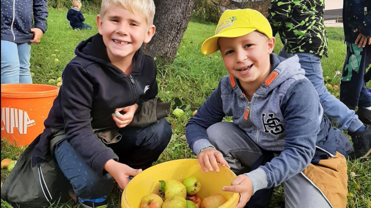 zwei Buben knien vor einem gelben Kübel mit Äpfeln